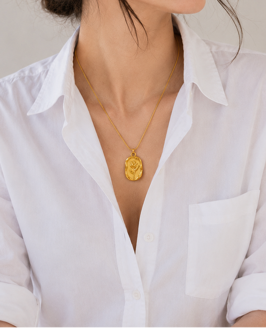 Woman wearing a white shirt and gold necklace against a plain background