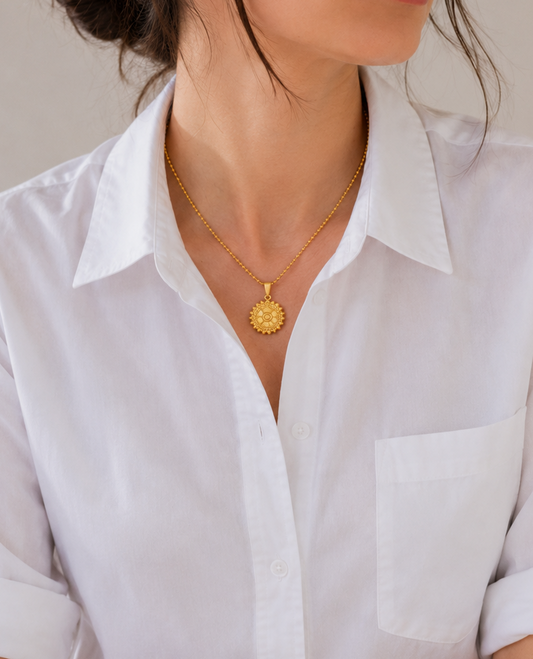 Woman wearing a white shirt and gold necklace against a neutral background