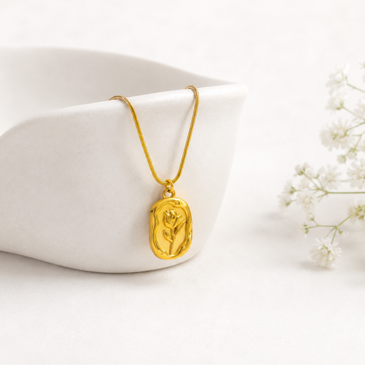 Gold necklace with a pendant on a white surface with white flowers